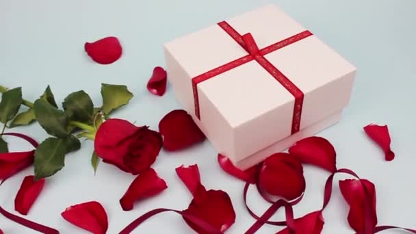 Piros rózsa és rózsaszirmok világos háttérrel... Valentin nap, szerelem koncepció. A férfiak kinyitnak egy fehér dobozt. vörös szív egy dobozban - Felvétel, videó