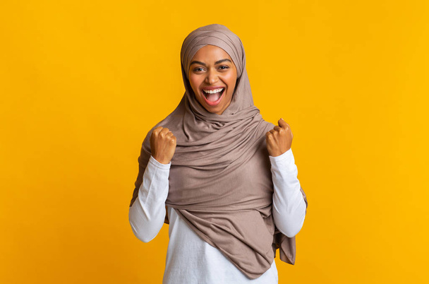 Black muslim woman in headscarf rejoicing success with raised fists - Фото, изображение