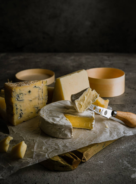 Variety of soft and hard cheeses, focus on brie cut with cheese knife. Low key image - Photo, Image