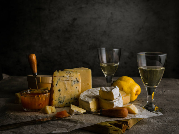 Low key still life with various cheeses, wine in glasses, quince fruit, and jam - Foto, imagen
