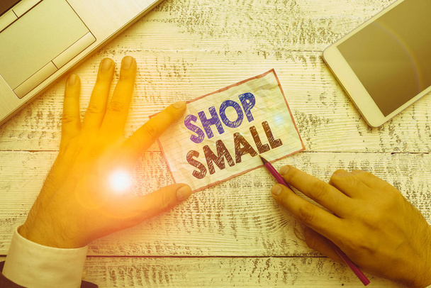 Word writing text Shop Small. Business photo showcasing nationwide movement that celebrates small businesses every day Hand hold note paper near writing equipment and modern smartphone device - Photo, Image
