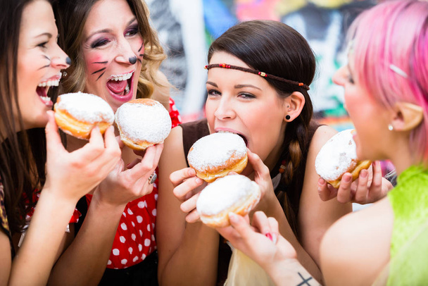 Chicas en el carnaval Fasching alemán comiendo pastelería tradicional tipo donut
 - Foto, Imagen