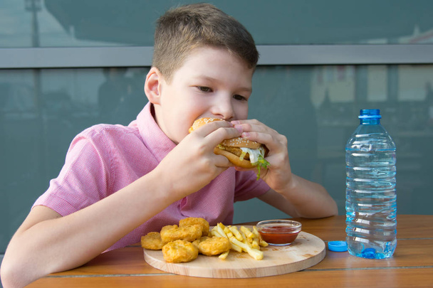 boy sitting at a table eating fast food and drinking water, close-up - Photo, image
