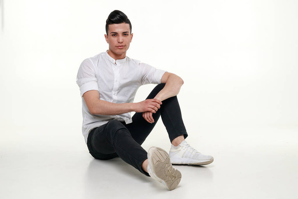 Handsome, young, trendy man is sitting on the floor in studio - Foto, afbeelding
