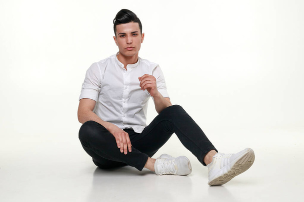 Handsome, young, trendy man is sitting on the floor in studio - Foto, Bild