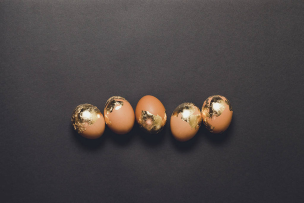 Easter greeting concept. Top view of golden decorated easter eggs on dark black background with copy space. - Photo, Image