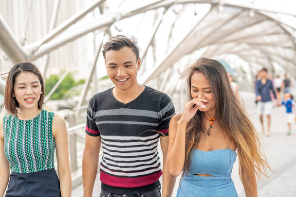 Üç Asyalı genç arkadaş şehirde yürüyor ve gülümsüyor. - Fotoğraf, Görsel