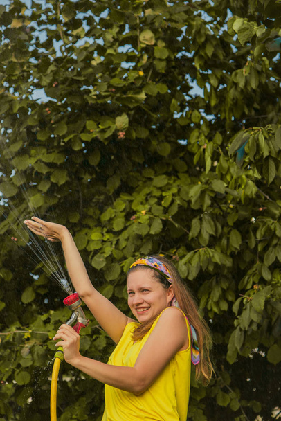 young pretty girl having fun in the garden watering plants with a hose. Smiling while taking a favorite hobby. - Foto, imagen