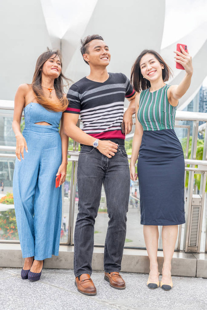 Trzech przyjaciół płci mieszanej spacerujących po mieście i robiących selfie. Koncepcja turystyki i wakacji. - Zdjęcie, obraz