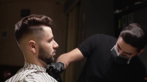 Confident hairdresser in black gloves shaving clients beard - Filmati, video