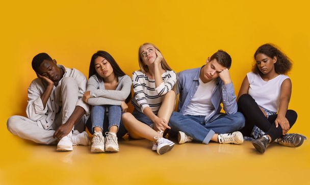 Βαρεμένοι συμμαθητές που κάθονται πάνω από κίτρινο φόντο, κουρασμένοι μετά τα μαθήματα - Φωτογραφία, εικόνα