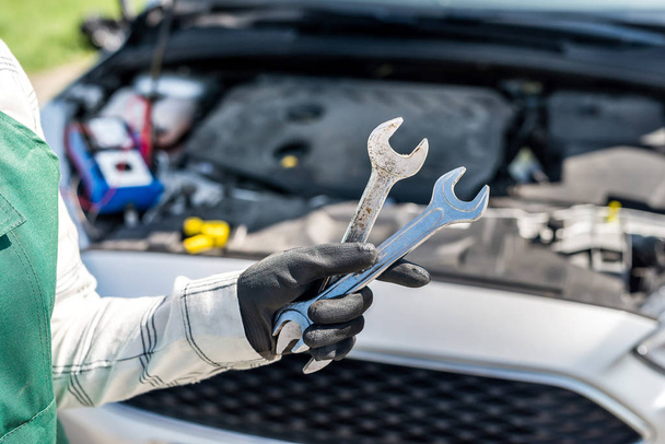 Different wrenches and spanners in hand over car engine - Photo, Image