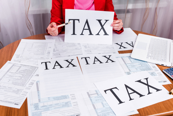 Жінка, що показує слово "податки" на аркуші паперу
 - Фото, зображення