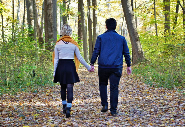 A young couple walking down a trail in the woods holding hands in the fall - Fotografie, Obrázek