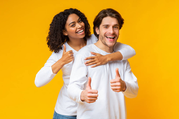 Retrato de feliz pareja interracial abrazando y gestos pulgares hacia arriba
 - Foto, imagen