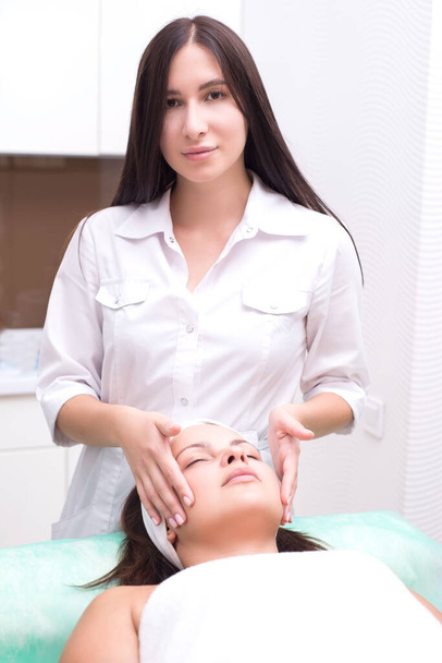 A massagista faz massagens faciais com uma mulher bonita. As mãos estão a fechar. Sala de massagem
 - Foto, Imagem