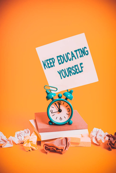 Text sign showing Keep Educating Yourself. Business photo showcasing dont stop studying Improve yourself using Courses Alarm clock sticky note paper balls stacked notepads colored background - Photo, Image
