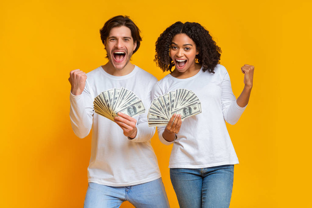Pareja interracial llena de alegría sosteniendo mucho dinero en efectivo, celebrando el éxito juntos
 - Foto, imagen