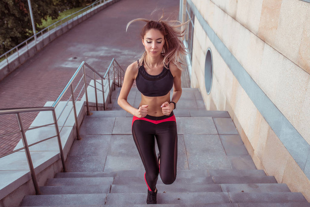 Beautiful girl jogging morning city running jump, staircase background, free space for copy text. Front view. Fitness training active lifestyle. Tanned athletic figure woman. Sportswear Leggings Top. - Foto, immagini