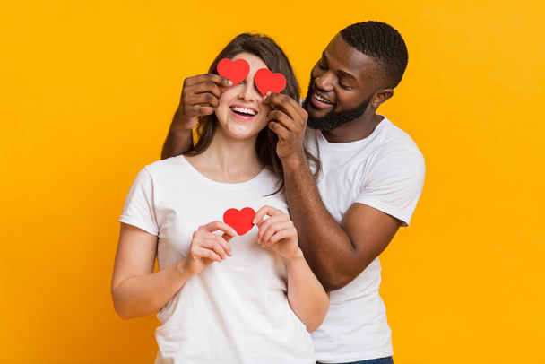 Cheerful Man Holding Red Paper Hearts Over His Girlfriends Eyes - Foto, immagini