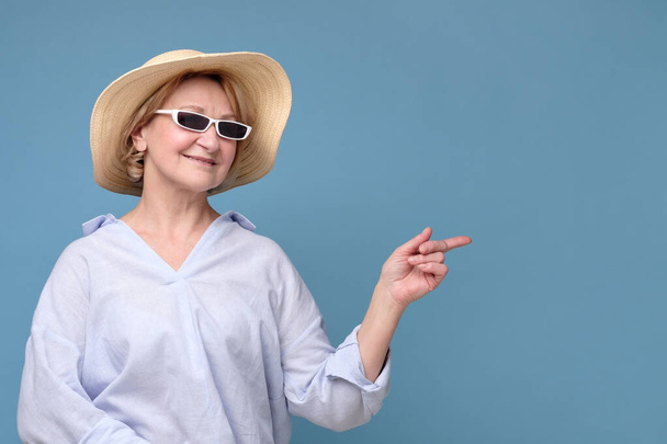 Woman insummer hat and sunglasses pointing aside having great mood smiling - Photo, Image