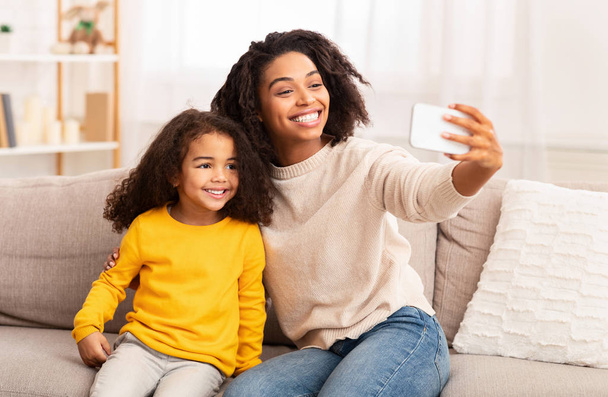 Moeder en dochter maken selfie zittend op bank thuis - Foto, afbeelding