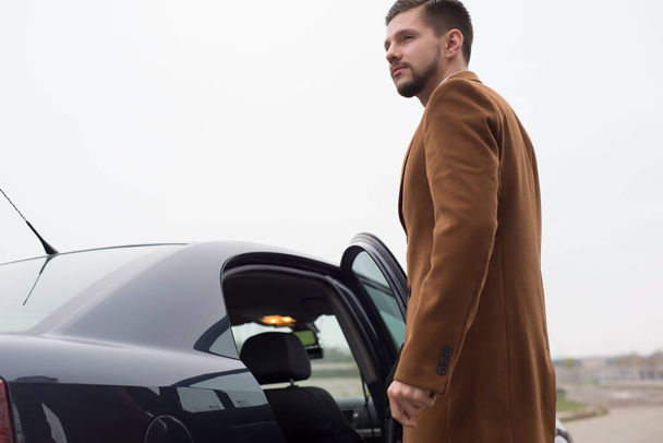 Portrait d'un jeune homme en tenue de travail, un homme d'affaires de trente ans ouvre la porte de la voiture à la sortie. Dans une création intéressante
 - Photo, image
