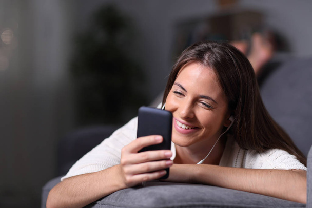 Happy teenage girl checking phone lying on a sofa in the night - Foto, imagen