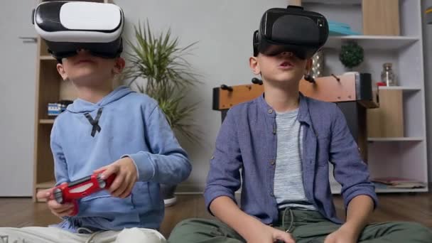 Good-looking modern teen boys sitting on the carpet and playing games using virtual reality headset and joysticks - Video, Çekim