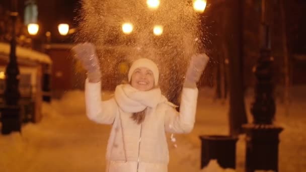 Mladá šťastná dívka vrhá sníh na noc město ulici - Záběry, video