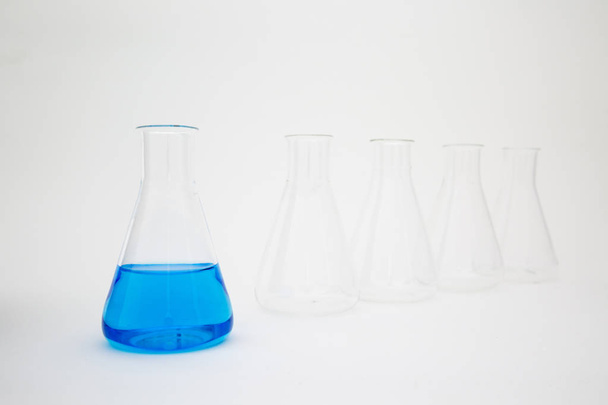 Laboratorní laboratorní skleněná Erlenmeyerova baňka naplněná modrou tekutinou se skleněným zařízením na bílém pozadí. - Fotografie, Obrázek