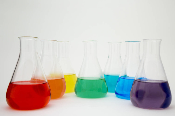 Laboratorium naukowe szkło erlenmeyer kolba wypełniona kolorowy płyn tworzący tęczę na białym tle. - Zdjęcie, obraz
