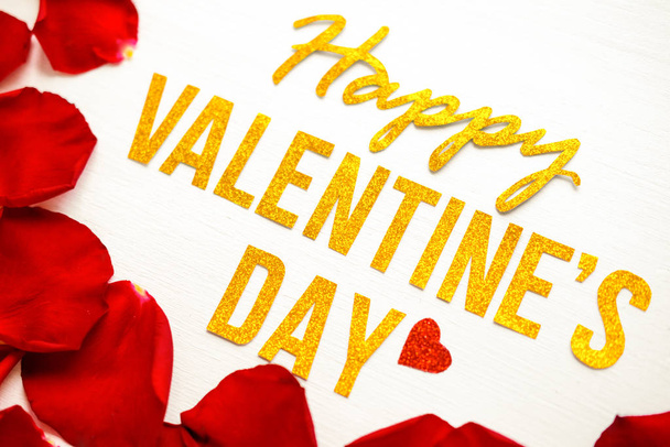 Happy Valentines Day gold text greeting card with red rose petals on white wooden background. romantic and Love concept - 写真・画像
