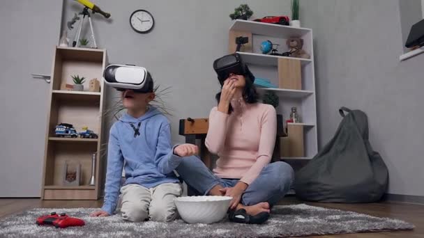 Attractive portrait of happy smiling modern mother and son which watching video movie using special virtual 3d glasses and eating popcorn at home - Imágenes, Vídeo