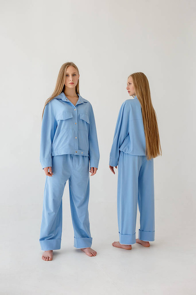 due sorelle gemelle con i capelli lunghi in posa in abiti oversize su sfondo bianco
 - Foto, immagini