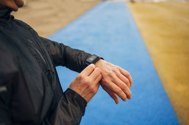 Atleta senior en ropa deportiva parado al aire libre en la calle y comprobando el tiempo en su reloj inteligente después de correr
 - Foto, Imagen