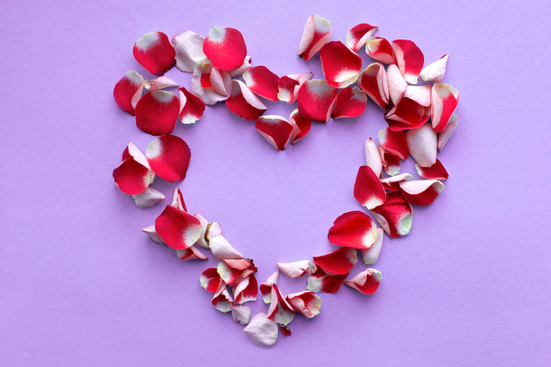 Pétalos de rosa roja en forma de corazón sobre fondo lila. Colores planos para tus elementos de diseño. Espacio para el texto. La vista desde arriba
 - Foto, imagen
