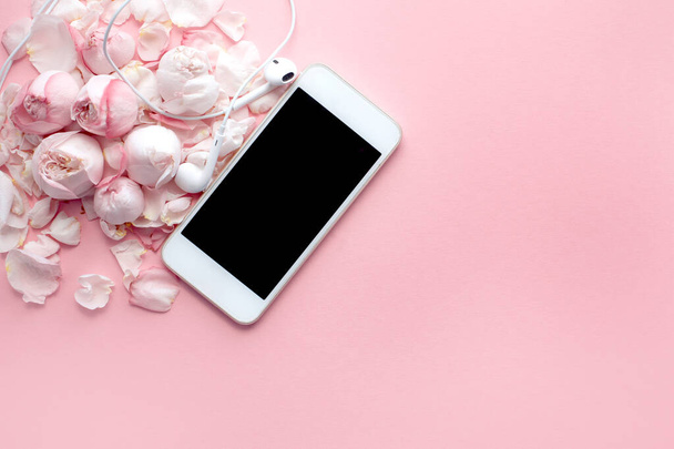 El teléfono inteligente blanco y los auriculares se encuentran en rosas y pétalos delicados sobre un fondo rosa, vista superior, posición plana. Espacio para texto, minimalismo
 - Foto, Imagen