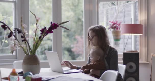 Single mother working from home and holding baby - Imágenes, Vídeo