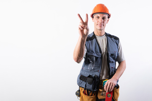 Builder shows a goat sign. In work clothes and hard hat. On a light gray background. - 写真・画像