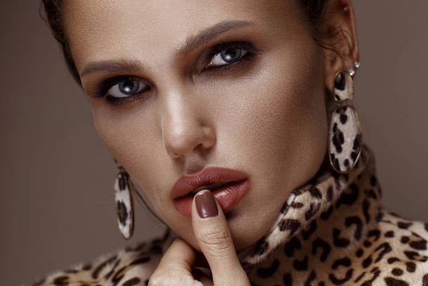 Beautiful sexy woman in a leopard coat and earrings, with classic smokey makeup and a fashionable hairstyle. Beauty face. - Photo, image