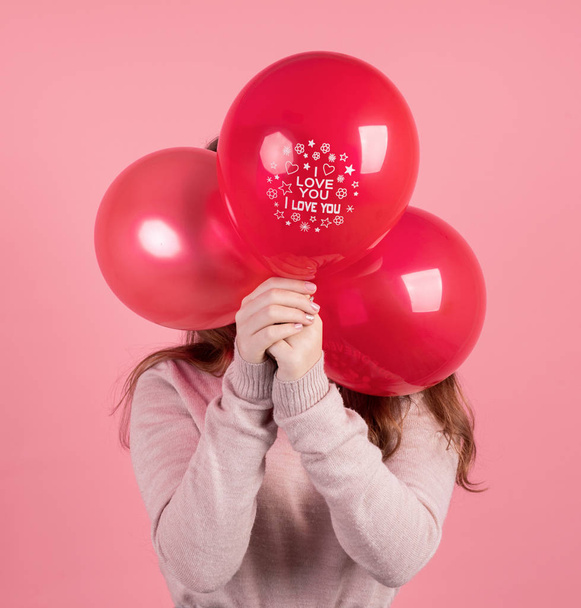 Woman covering her face with three red balloons with the words I Love You isolated on pink background - 写真・画像