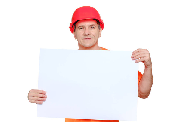 Retrato sonriente trabajador guapo de mediana edad con sombrero rojo duro, mirando a la cámara y sosteniendo hoja de papel en blanco
 - Foto, Imagen