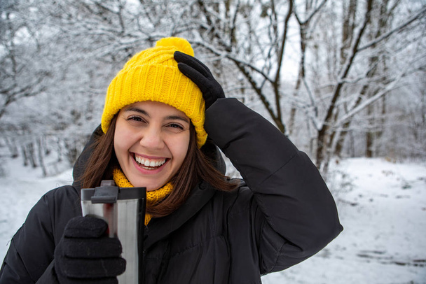 smiling woman in winter outfit drinking warm up drink from refillable mug - Photo, Image