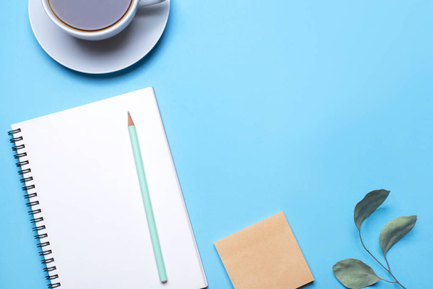 Blue background with notepad, pencil and cup of coffee. - Фото, изображение