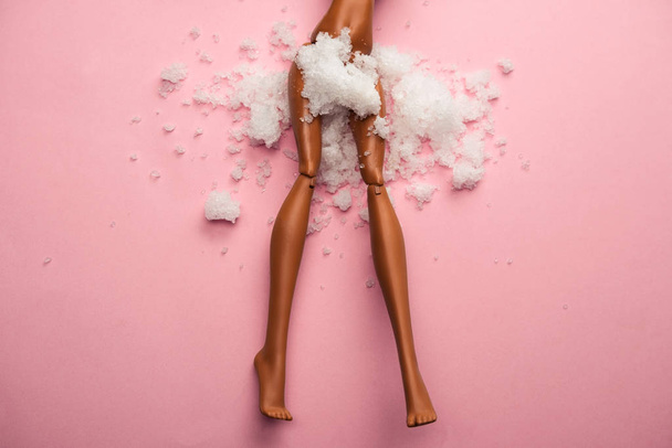 plastic doll legs with snow covered  crotch on  pastel pink background - Foto, afbeelding