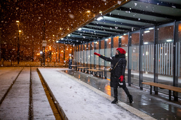 Frau blickt auf Schnee, der in der Winternacht an der Straßenbahnhaltestelle steht - Foto, Bild