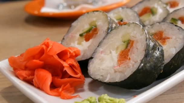 Large sushi rolls in a nori with salmon, crab sticks, cucumbers, philadelphia cheese. Nearby is green wasabi and red ginger. Japanese food - Footage, Video