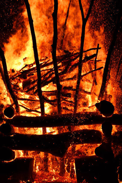 Niesamowite ognisko ogniska w wiosce w ciemną noc. Spalanie drewna opałowego tworzy duże płomienie, rozbłyski, dym, gaz i generuje szerokie światło wokół ognia. Zdjęcie pionowe. - Zdjęcie, obraz