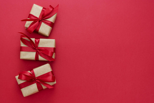 Gift boxes wrapped with kraft paper and red bow isolated on red background. Abstract flat lay. - Valokuva, kuva